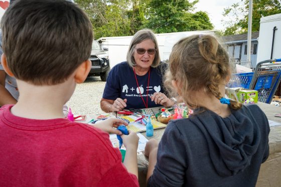 An adult sitting at a table helping two children do an art making activity.